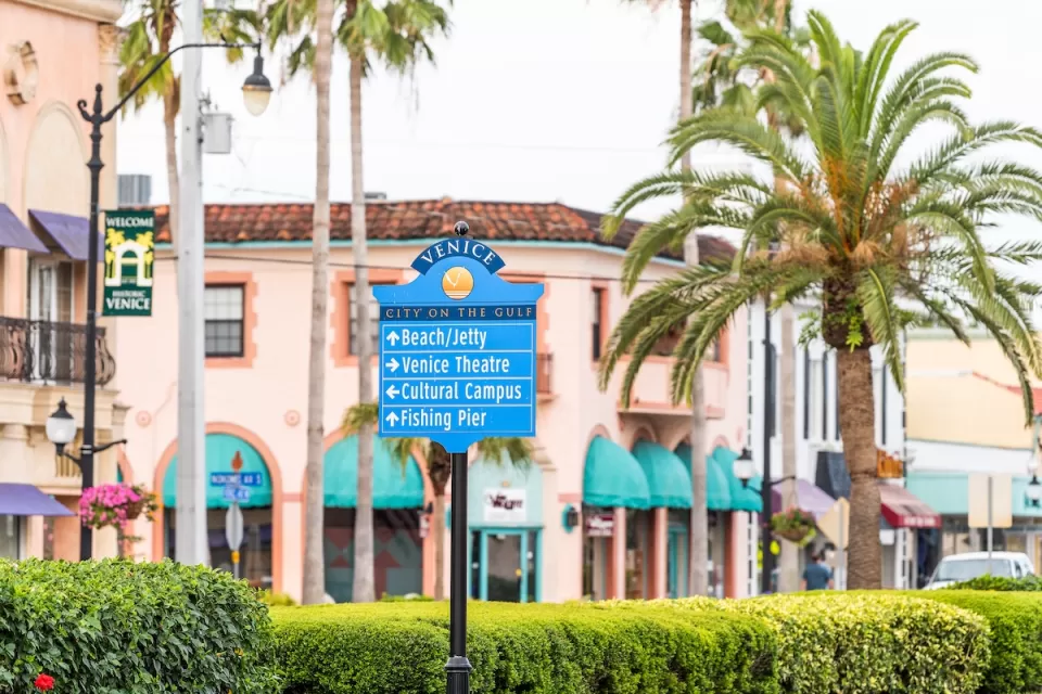 Street sign in Venice, Florida planned community with pink Italianate buildings and palm trees in background.